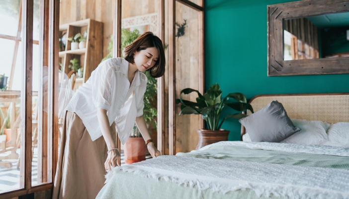 A young woman makes her bed at home with layers.