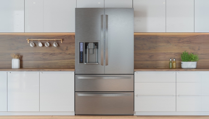 A stainless steel refrigerator in a white and natural wood kitchen.