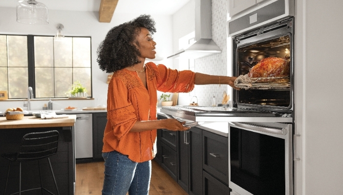 A woman removes a turkey from her double wall oven at home. 