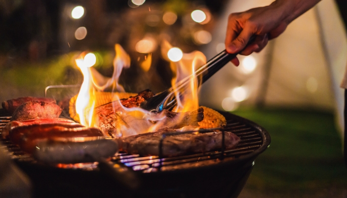 A male hand flips food on a charcoal grill. 