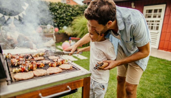 A man and child flip food on an outdoor grill together.