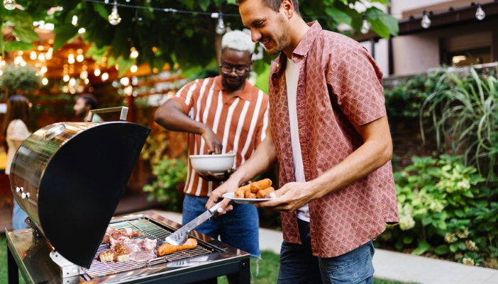 Two friends grill outdoors together on a summer evening.