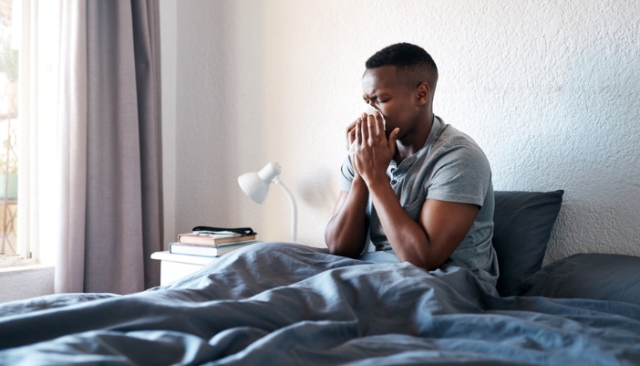 A man sneezes in his bed due to allergies.