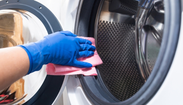 A hand with a pink glove wipes off the interior of a laundry appliance.