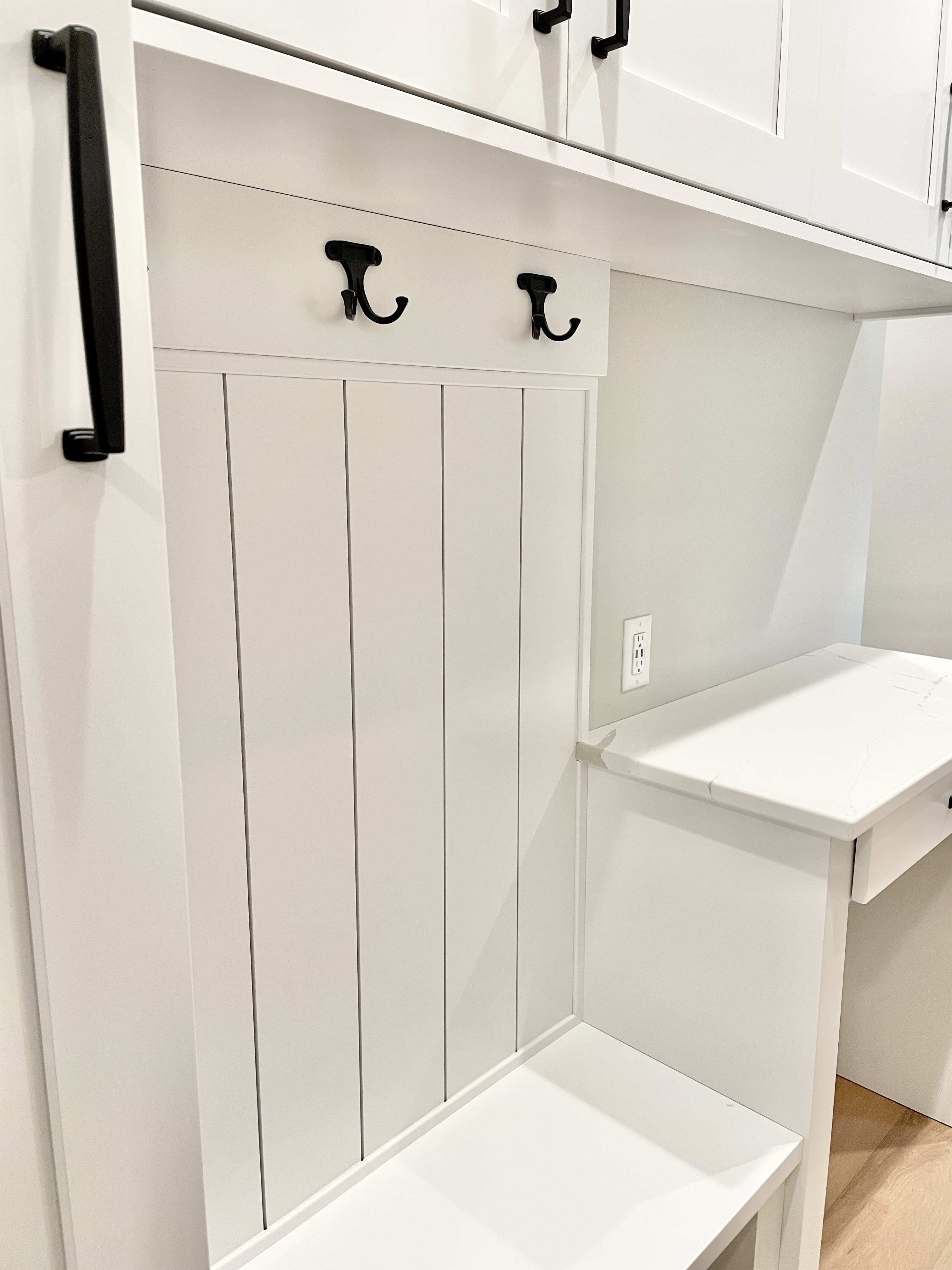 white beaded panel with black coat hooks in mudroom locker area
