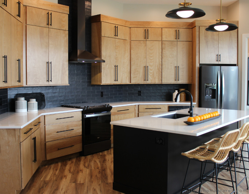 view of kitchen design with black island and birch cabinets with black wall tile and black stainless appliances
