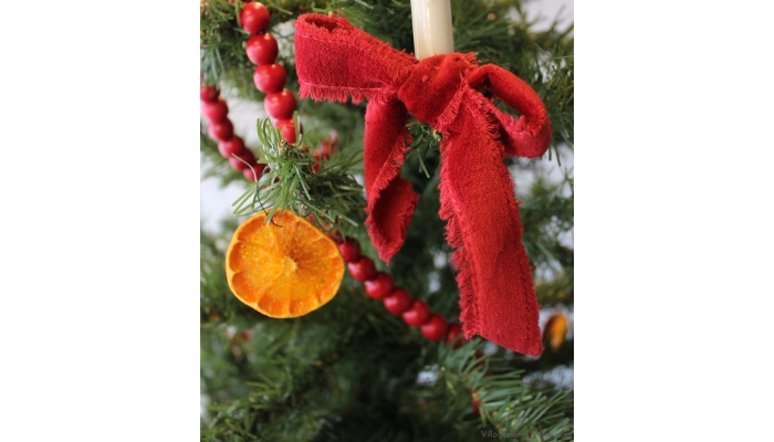 closeup of Christmas tree with dried orange slices, candle lights draped red bows, and cranberry garland.