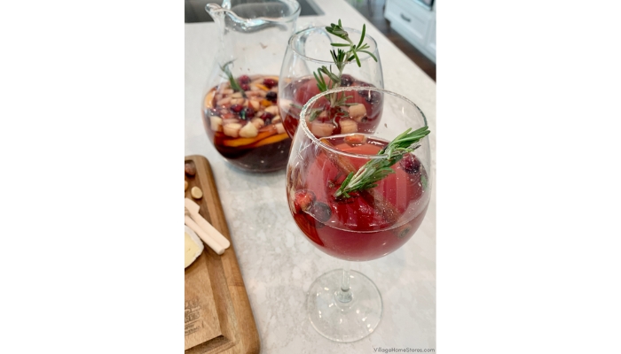 two glasses or red sangria with fruit and rosemary garnishes on white marble look countertops