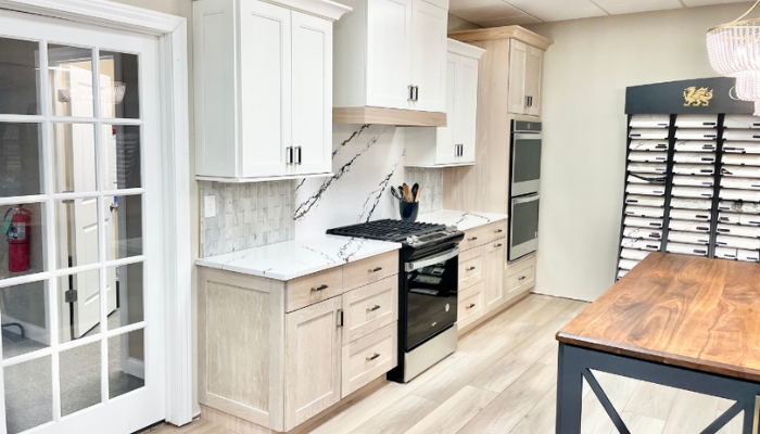 Cabinet display in the village showroom with white oak bases and painted white upper cabinets installed with light oak vinyl plank flooring and cambria quartz countertops.