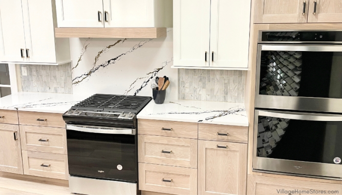 cooking zone of kitchen with gas range and double wall oven. Light oak base cabinets and painted linen white upper cabinets featured with Cambria quartz Oakleigh counters and full height splash behind the cooktop.