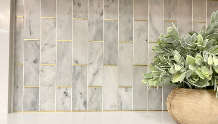 close up image of marble wall tile with gold accent details in grout lines. Light wood vase with green succulent on right
