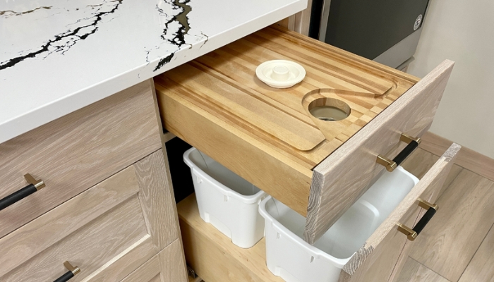 light oak base cabinet with pull out trash bin shown open with cutting board drawer above. 