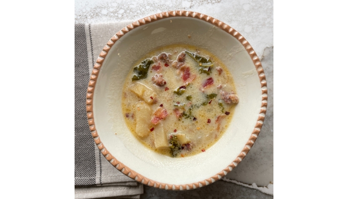Overhead view image of zuppa tuscana soup in a ceramic bowl topped with bacon and red pepper flakes.