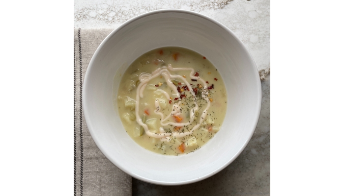 Overhead view image of creamy dill pickle soup in a bowl topped with dill, red pepper flakes, and siracha sour cream.