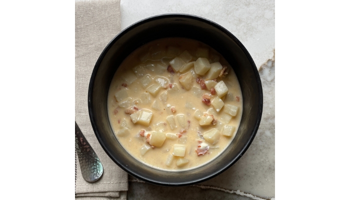 Overhead view image of potato soup in a black ceramic bowl.
