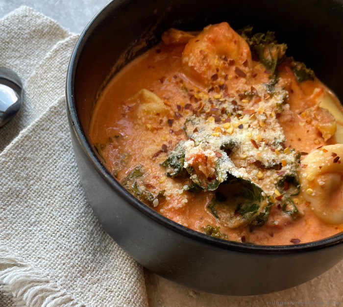 creamy tomato chicken and cheese tortellini soup in a bowl topped with red pepper flakes.