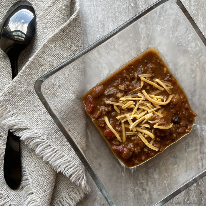 Overhead view image of square glass bowl of chili with shredded cheese on top