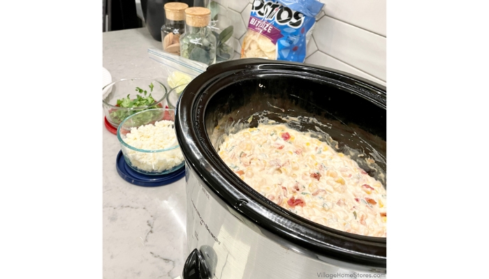 Crockpot filled with corn dip and bowls of garnish on counter