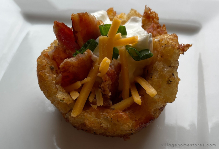 close up of loaded tater tot bowl on white plate topped with bacon and green onion