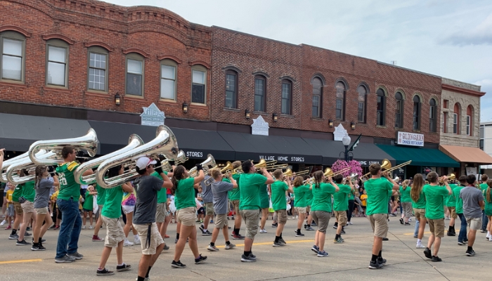 exterior of three storefronts and awnings that form village home stores downtown Geneseo, Illinois. Marching band with green t-shirts marching by in front of store
