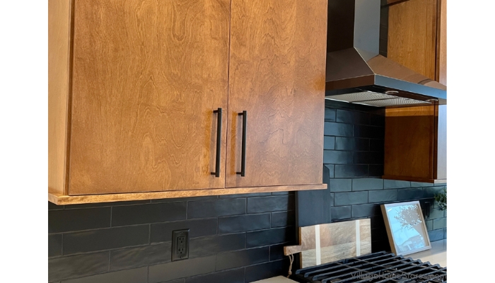 kitchen wall cabinet in slab style, birch wood and medium briarwood stain. Black stainless chimney range hood in background