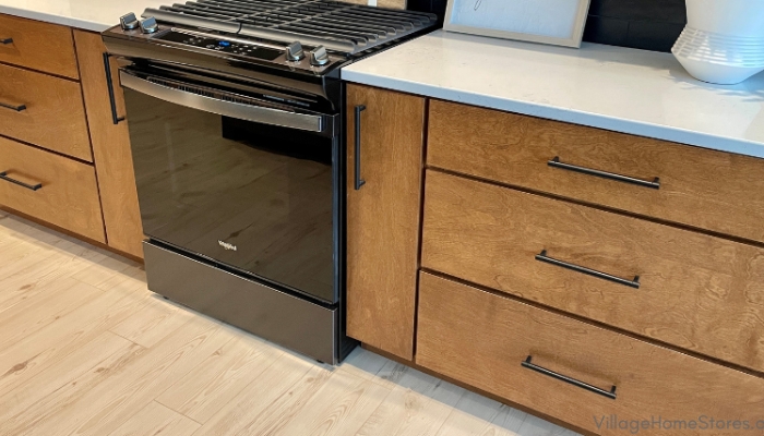 Koch cabinetry in birch wood and briarwood stain. Black stainless gas range installed with white quartz countertops.