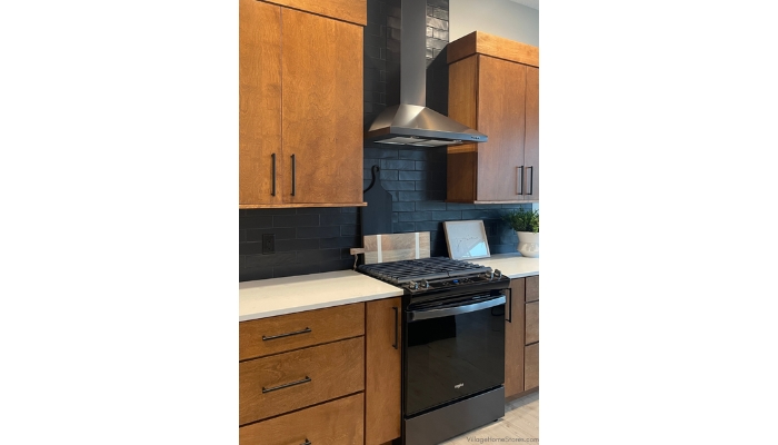 black stainless steel gas range with black range hood installed with birch cabinetry and black wall tile