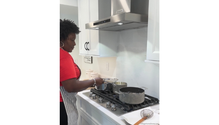 Chef Keys at gas cooktop in white painted kitchen with Silestone backsplash and stainless steel range hood for ventilation