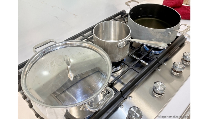 5-burner stainless steel cooktop with three pans on it and burners on