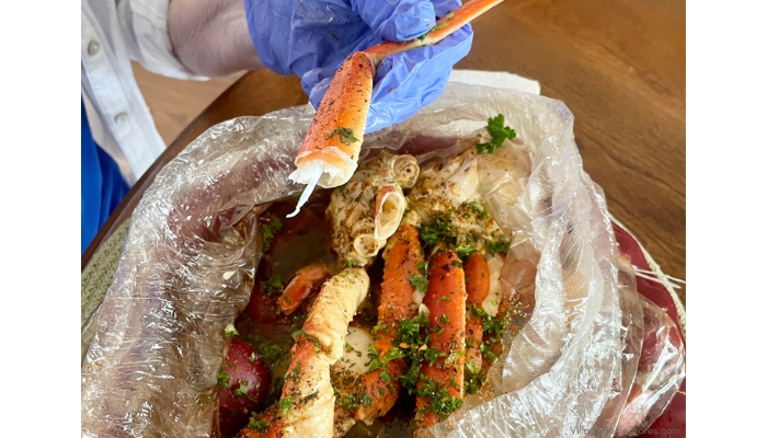 Cajun seafood boils shown finished and open with blue gloved hands holding crab leg