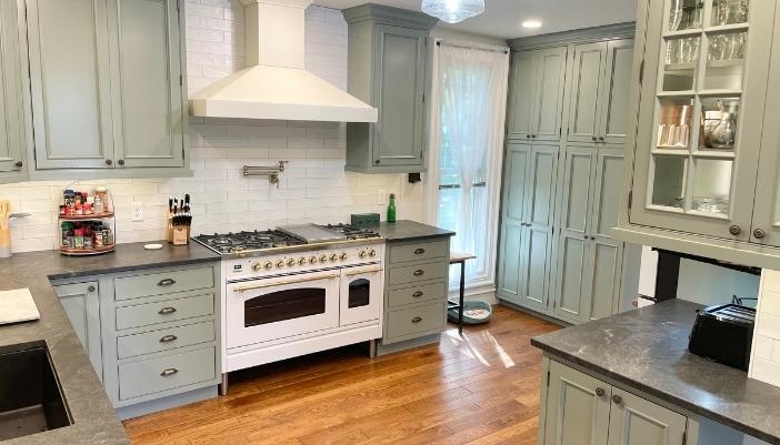 light sage green painted kitchen with hardwood floors and white appliances. Cabinetry in evergreen fog paint from Village Home Stores