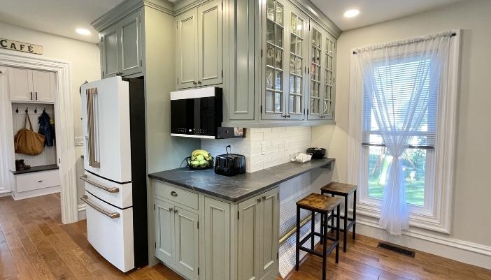 light sage green painted kitchen cabinets with mullion glass doors and white appliances. Cabinetry in evergreen fog paint from Village Home Stores