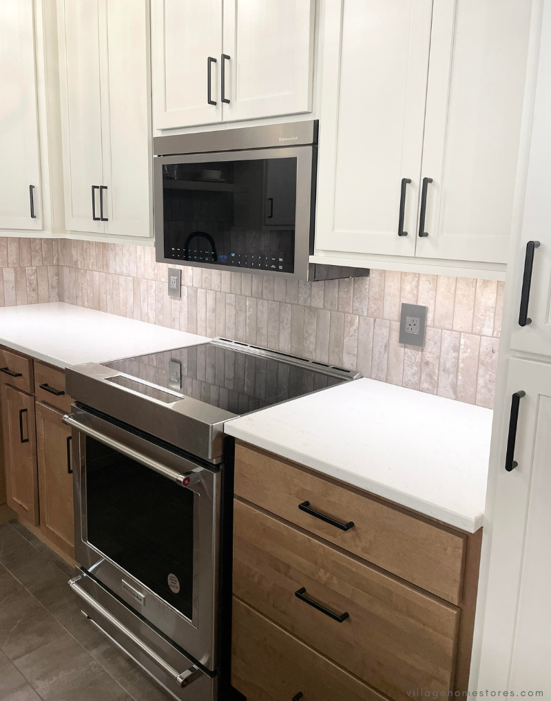 Stainless steel kitchenaid appliances in a white and maple kitchen including an induction range and flush over range microwave hood