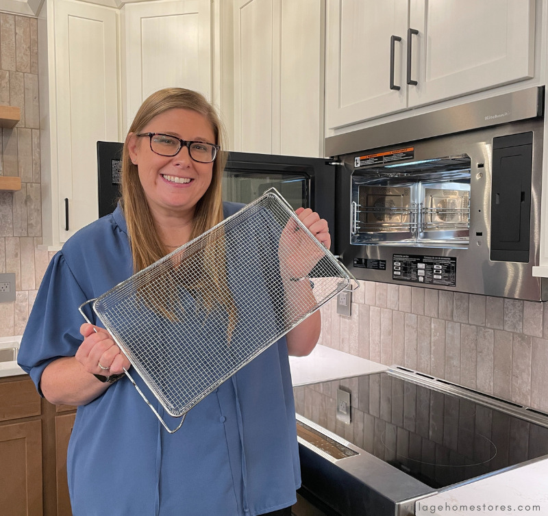 woman in blue shirt holding metal air fry tray next to open microwave appliance door