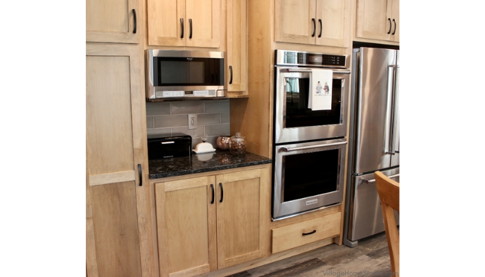 Light wood cabinet kitchen with stainless steel appliances including an over the counter microwave installed above dark stone countertops