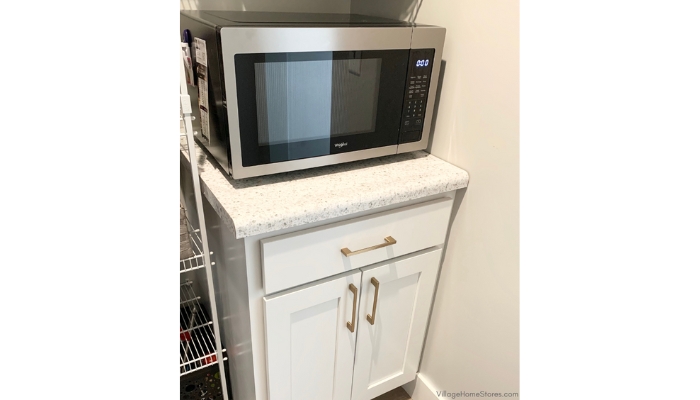 Stainless countertop microwave on small cabinet in kitchen pantry area
