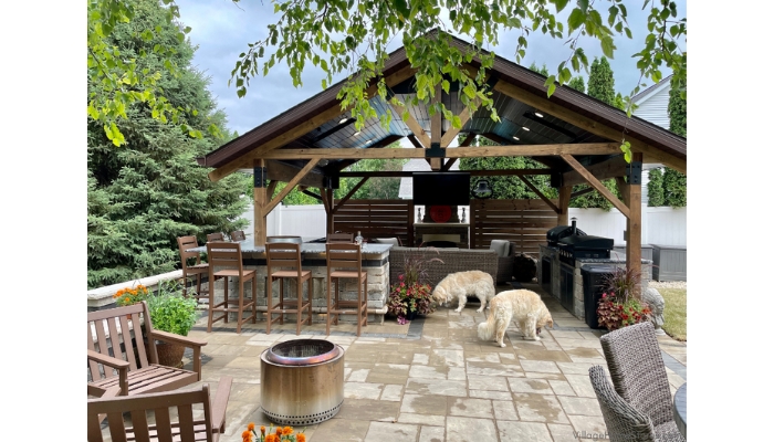 outdoor covered patio area with bar kitchen and living room space. Two dogs on paved courtyard