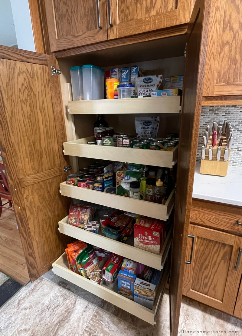 tall oak pantry cabinet with slide out shelves inside shown with pantry doors open.