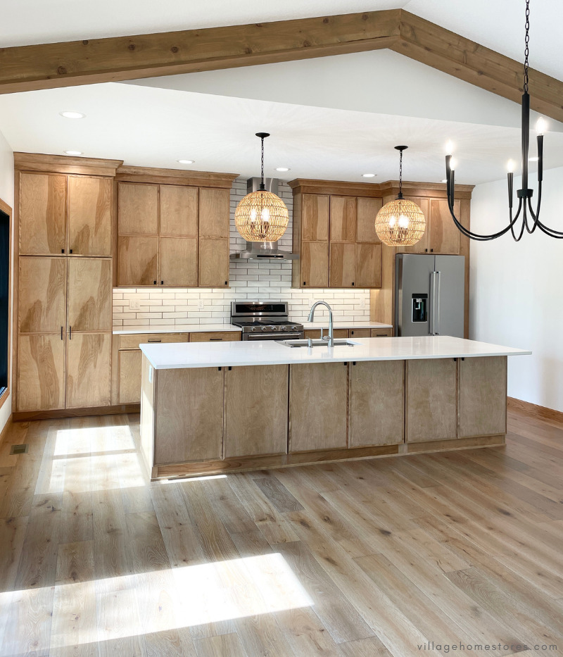 great room kitchen with large island, medium wood cabinets and flooring, and woven pendants above