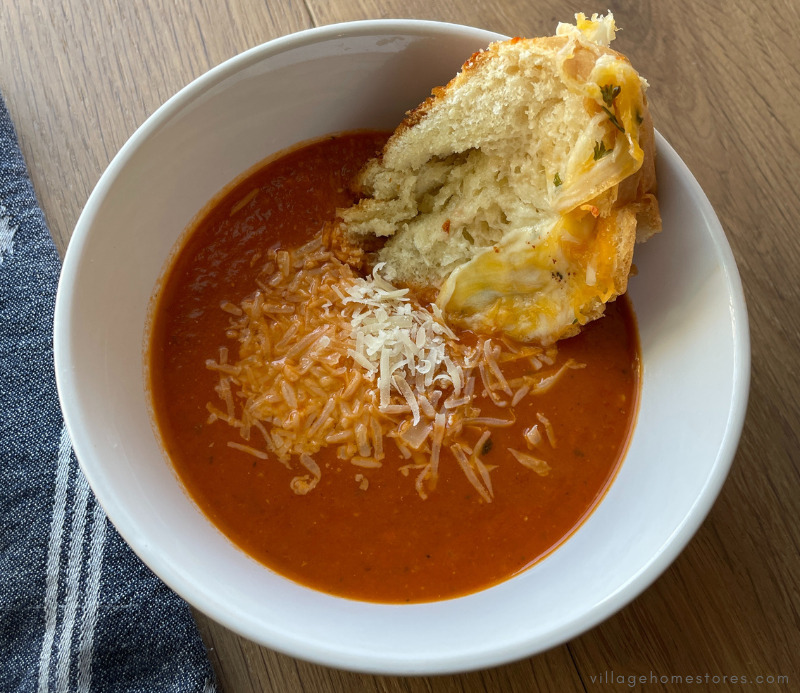white bowl of tomato basil soup with slice of garlic bread in it