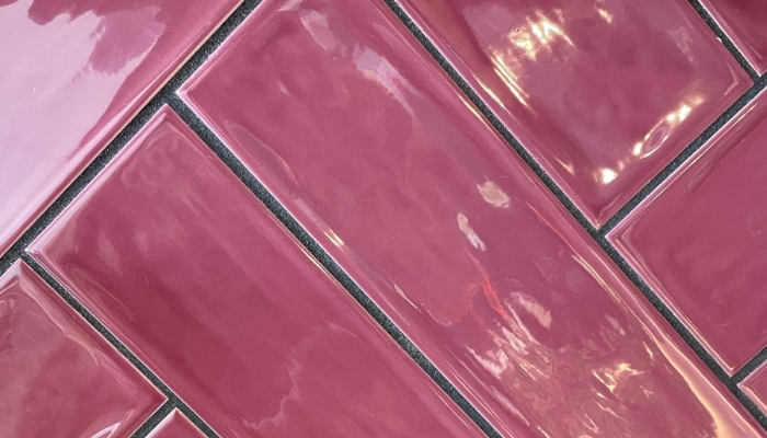 close up image of long burgundy gloss wall tile installed in a herringbone pattern