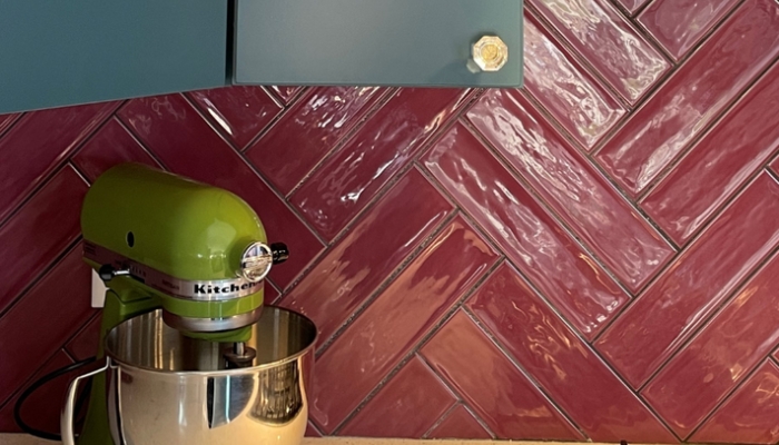 colorful kitchen with teal cabinets, bright green kitchenaid mixer, and glossy burgundy maroon wall tile as backsplash