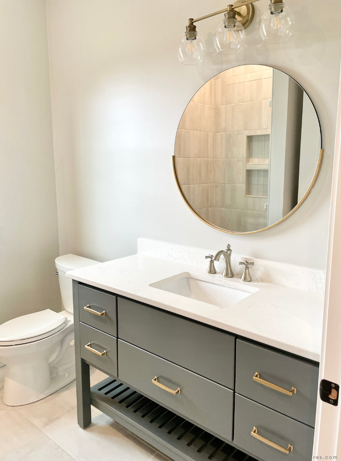 Bertch bath interlude sink vanity with circle mirror above reflecting tiled shower and midcentury vanity light above