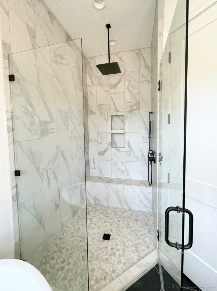white and gray tiled shower with bench seat, glass door entry, and matte black rain showerhead
