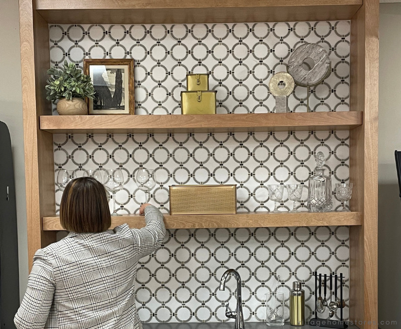 Image of Beth Nordby styling open shelves in wet bar display with brass and gray decor