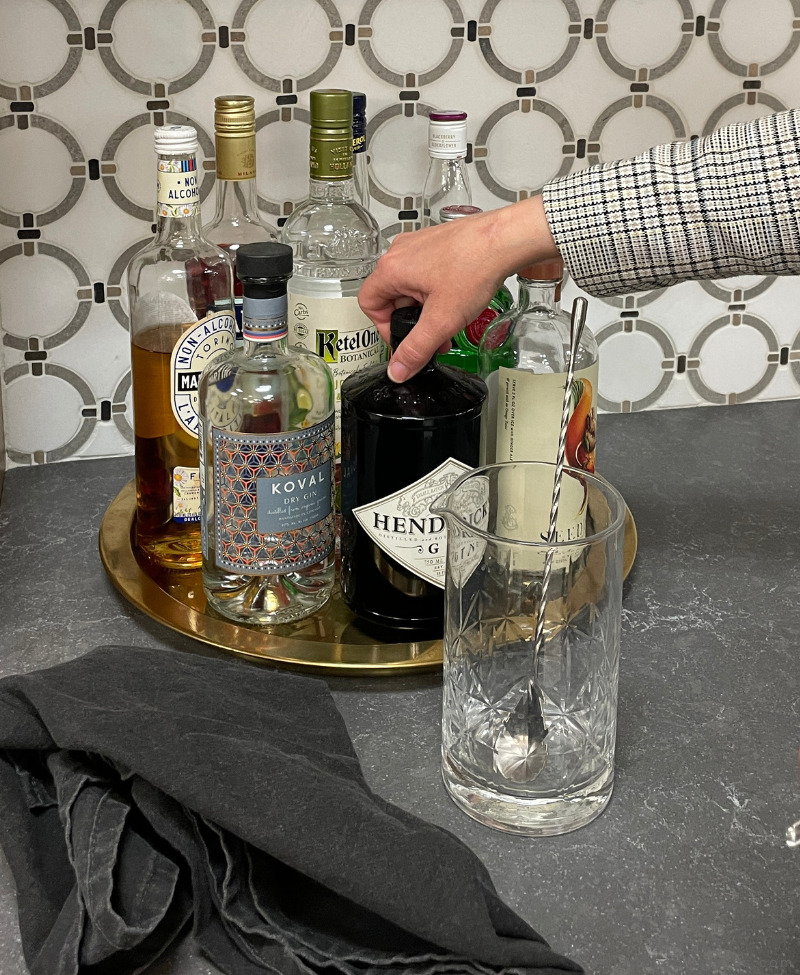 arm reaching in to grab gin bottle from brass tray