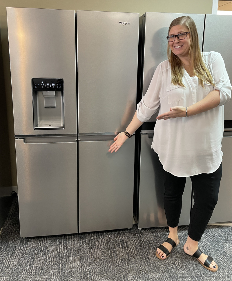 woman in white blouse pointing to stainless steel 4 door refrigerator with water dispenser