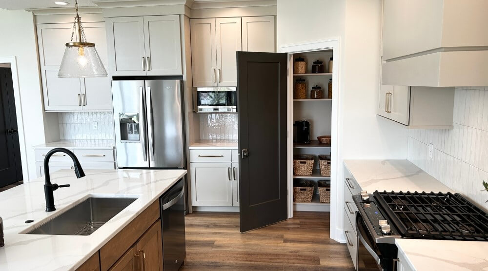 accessible beige kitchen cabinets with stainless refrigerator and corner pantry door open