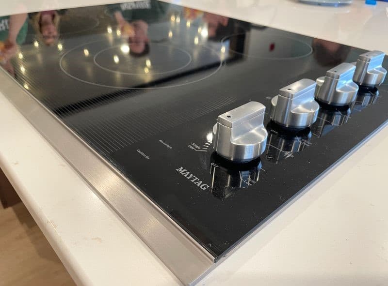 close up of black glass electric cooktop with stainless knobs and Maytag logo