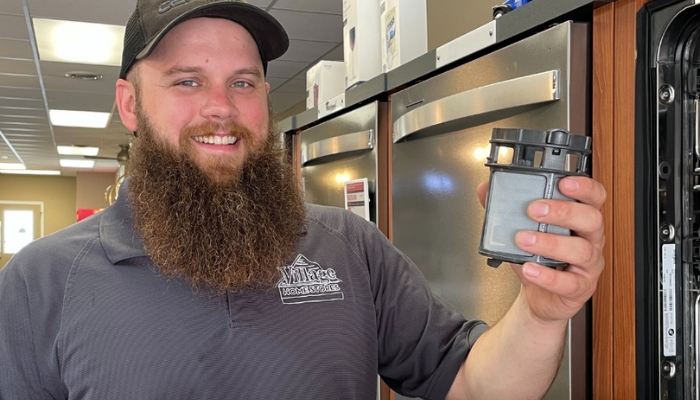 ervice technician with blue village home stores polo holding dishwasher filter next to open dish washer 